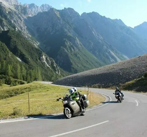 Motorrijders op een bergweg door een groene Alpenvallei