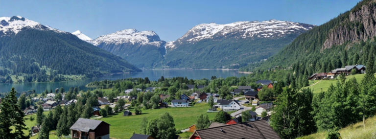 Noors landschap met een idyllisch dorp, fjord en sneeuwtoppen tijdens een motorvakantie noorwegen.