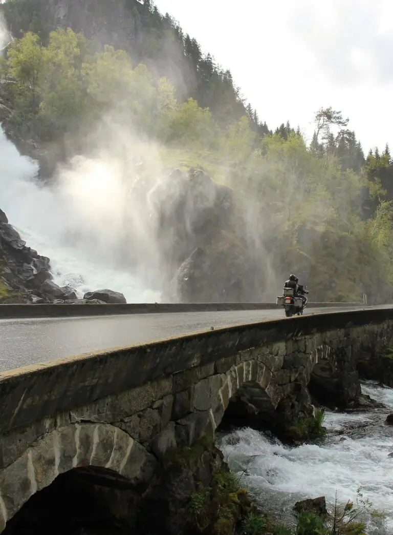 Motorrijder op stenen brug tijdens motorvakantie Noorwegen langs een waterval.