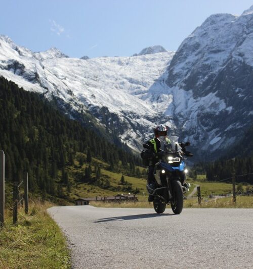 Motorrijder in een Alpenvallei met besneeuwde bergtoppen