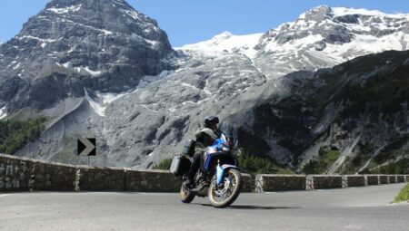 Motorrijder voor een gletsjer en besneeuwde Alpen