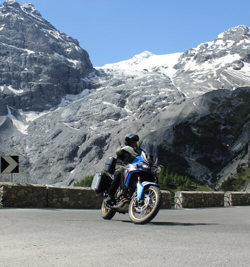 Motorrijder voor een gletsjer en besneeuwde Alpen
