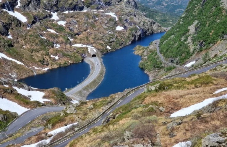 Kronkelende bergweg met tunnel langs een blauw bergmeer en sneeuwvelden in de Noorse bergen.